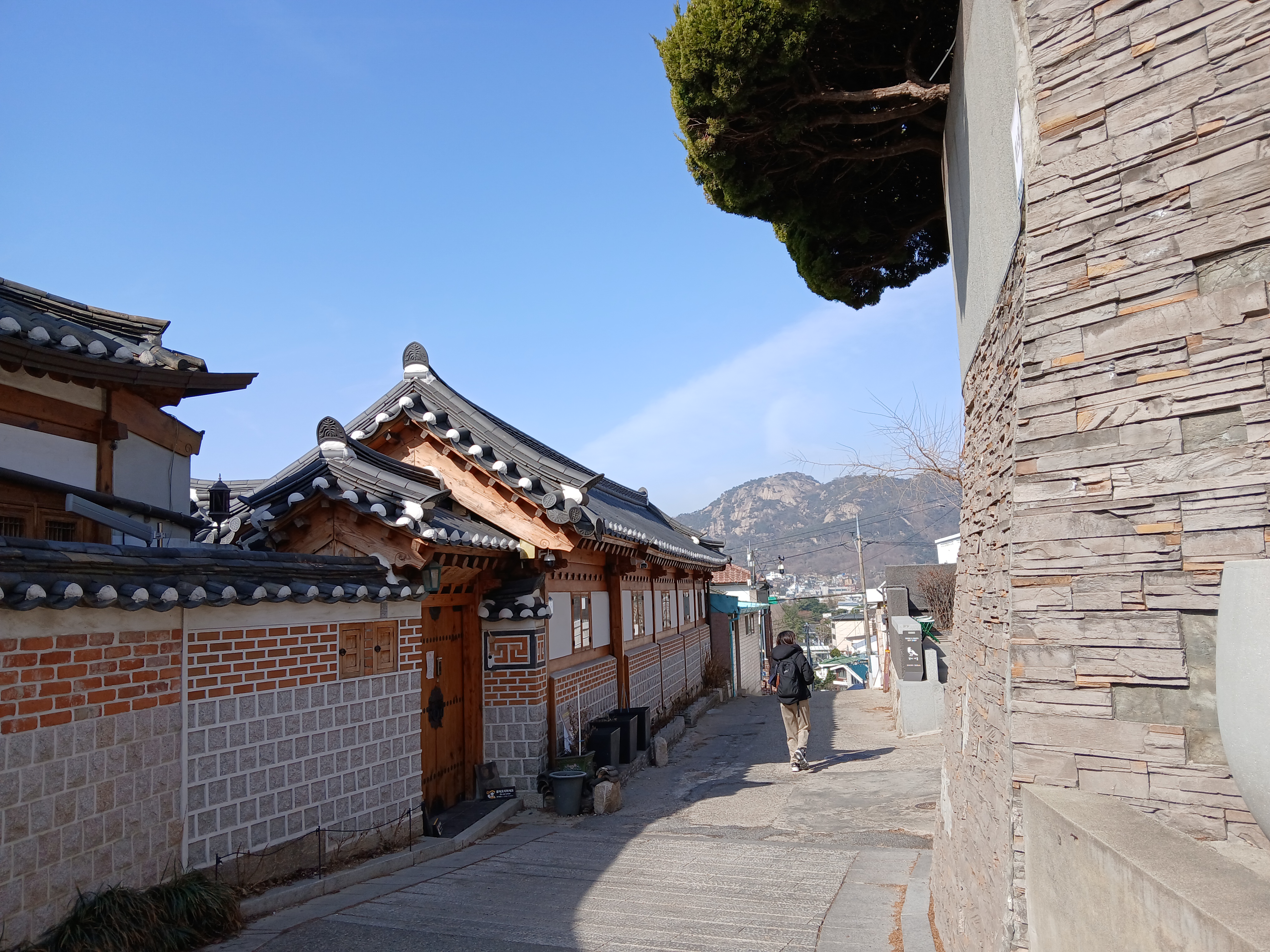 기와지붕과 벽돌 담장이 이어지는 북촌 골목, 멀리 산이 보이는 풍경